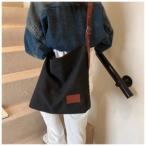 Detailed shot of a large black canvas tote bag with adjustable brown leather shoulder strap