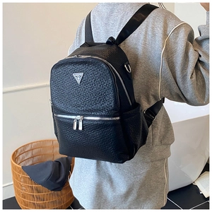Détail d'un sac à dos en cuir noir gaufré avec un logo triangulaire en métal argenté