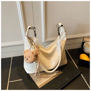 Detail of cream hobo bag with crocodile pattern and plush bear charm pendant