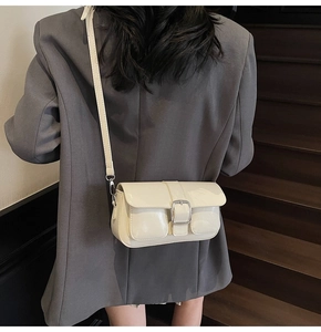 Close-up of a glossy cream small square bag with silver buckle worn on a grey blazer