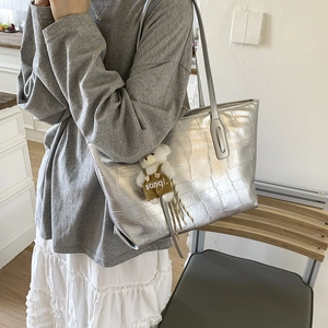 Detail of silver tote bag featuring crocodile embossed texture and plush bear charm