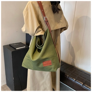 Close-up of a large green canvas tote bag featuring a leather strap and logo patch