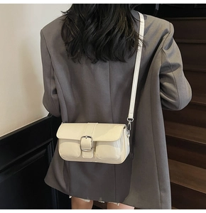 Detail of glossy cream patent leather crossbody bag with silver buckles and dual front pockets