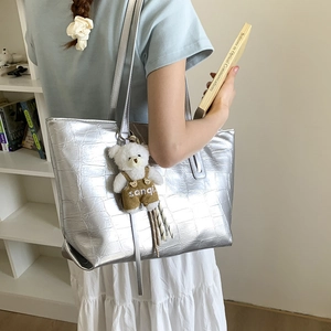Detail of silver crocodile pattern tote bag with teddy bear charm on shoulder strap