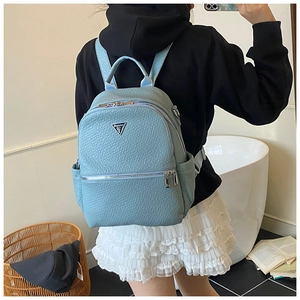 Détail du sac à dos en cuir texturé bleu clair avec logo triangulaire en métal à l'avant