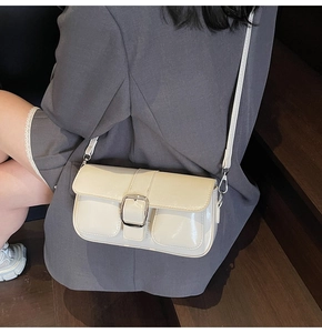 Detail shot of a cream square crossbody bag with a silver buckle on a gray suit outfit
