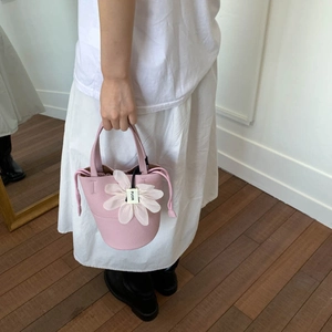 Detail of pink pebbled leather bucket bag with white floral pendant and drawstring