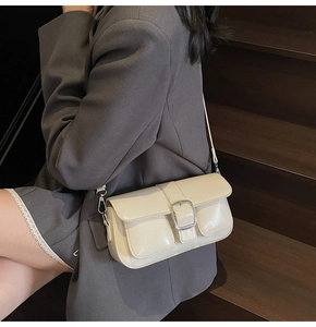 Detail of a beige flap crossbody bag with metal buckle and two front pockets on a model