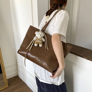 Detailed view of deep brown crocodile pattern tote bag with white plush bear charm