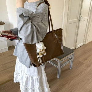Detail of dark brown faux crocodile leather tote bag with a small plush bear charm