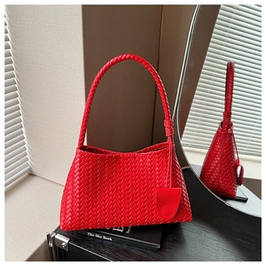 Detail of red woven leather handbag with matching charm on a stylish wooden desk