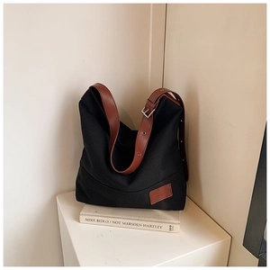 Detail view of black canvas tote bag showing adjustable brown faux leather straps and logo