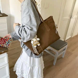 Brown crocodile texture tote bag with plush bear charm worn by a model in interior