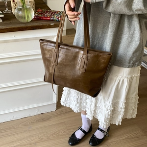 Detail of dark brown faux leather tote bag with elegant crocodile pattern and slim handles