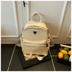 Détail d'un sac à dos beige gaufré avec logo triangulaire noir et fermetures éclair