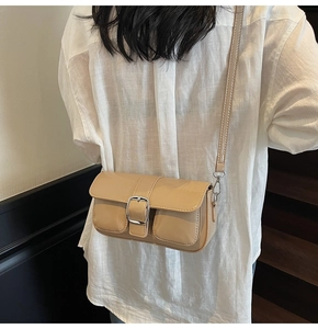 Detailed view of cream patent leather crossbody bag with silver buckle worn by model