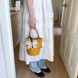 Detail of yellow lychee leather bucket bag with a large white floral charm accessory