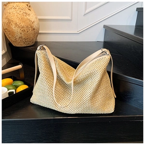 Détail d'un sac cabas tissé beige avec des anses en cuir sur un escalier en bois
