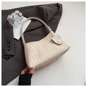 Detail of cream-white woven underarm bag with snap closure in an elegant lifestyle setting