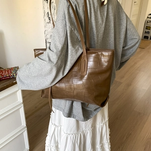 Detailed close-up of brown crocodile texture on premium leather tote bag worn by a model