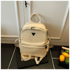 Détail du sac à dos blanc crème à texture ondulée avec logo triangulaire en métal noir