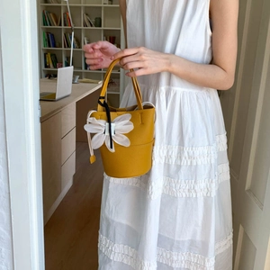Detail of yellow bucket bag with lychee leather texture and a large white fabric flower charm