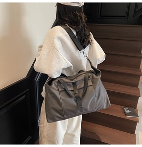 Deep grey nylon travel bag shown on shoulder in a stylish indoor setting with stairs