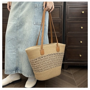 Detail of hollow woven straw tote bag with brown leather handles on denim background