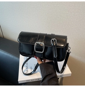 Detail of black glossy leather shoulder bag featuring a large silver buckle and two front pockets