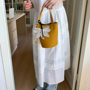 Detail of yellow lychee leather bucket bag featuring a white 3D flower petal charm