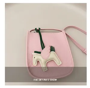 Close-up of pink lychee leather bucket bag with cream pegasus charm on a brown blazer