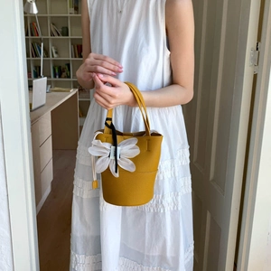 Detail of yellow lychee leather bucket bag with large white flower charm on strap