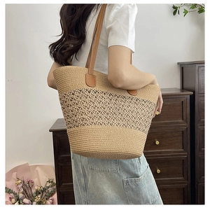 Detail of hollow-out straw tote bag featuring brown leather handles and woven texture