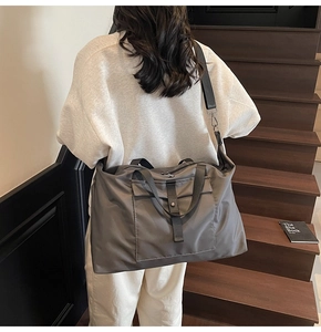Side view of a large grey waterproof travel bag with adjustable strap on wooden stairs