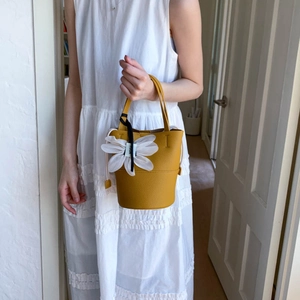 Close-up of a yellow bucket bag with a large white 3D flower and monochrome ribbon charm