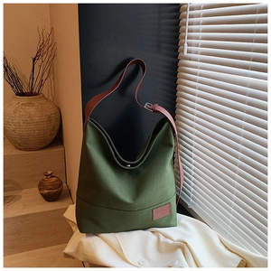 Detail of olive green canvas tote bag showing metal snap closure and leather tag