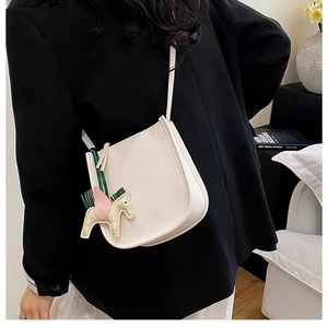 Close-up of a white lychee grain saddle bag with a horse pendant on a fashion model