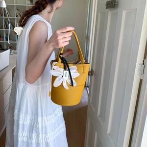 Detail of yellow pebbled leather bucket bag featuring floral charm and FUOR ribbon