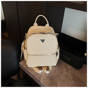 Détail du sac à dos beige en similicuir montrant la texture grainée et le logo en métal