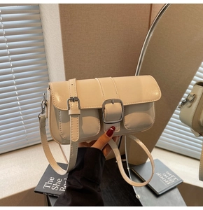 Detail of a creamy beige glossy leather crossbody bag featuring a large metal buckle