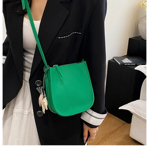 Detail of green litchi leather crossbody bag with a cute elephant charm accessory