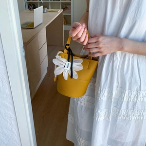 Detail of yellow lychee leather bucket bag with white floral charm held by model