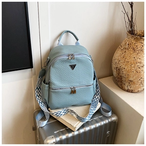 Détail d'un sac à dos bleu clair en cuir texturé avec plaque métal et bandoulière tissée