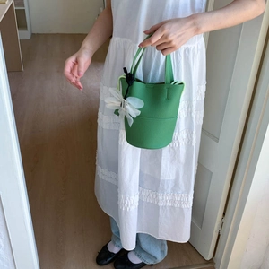 Detail of green bucket bag in pebble leather with a white tulle floral charm accessory