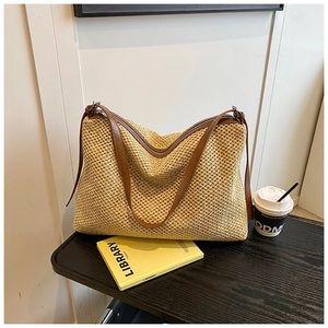 Détail d'un sac cabas en paille tressée avec lanières en cuir brun et fermeture éclair