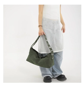Detail of dark green tote bag featuring metallic grommets on a wide shoulder strap