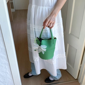 Detailed shot of bright green bucket bag featuring lychee grain leather and silk flower charm