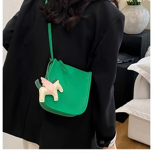 Detail of green leather shoulder bag with a colorful winged horse charm and textured finish