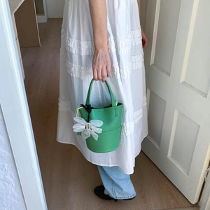 Close-up of a bright green bucket bag with a white mesh flower charm and lychee texture