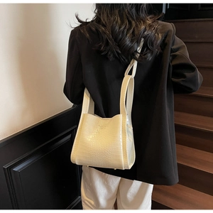 Detail of cream crocodile embossed handbag with wide strap shown on model over shoulder